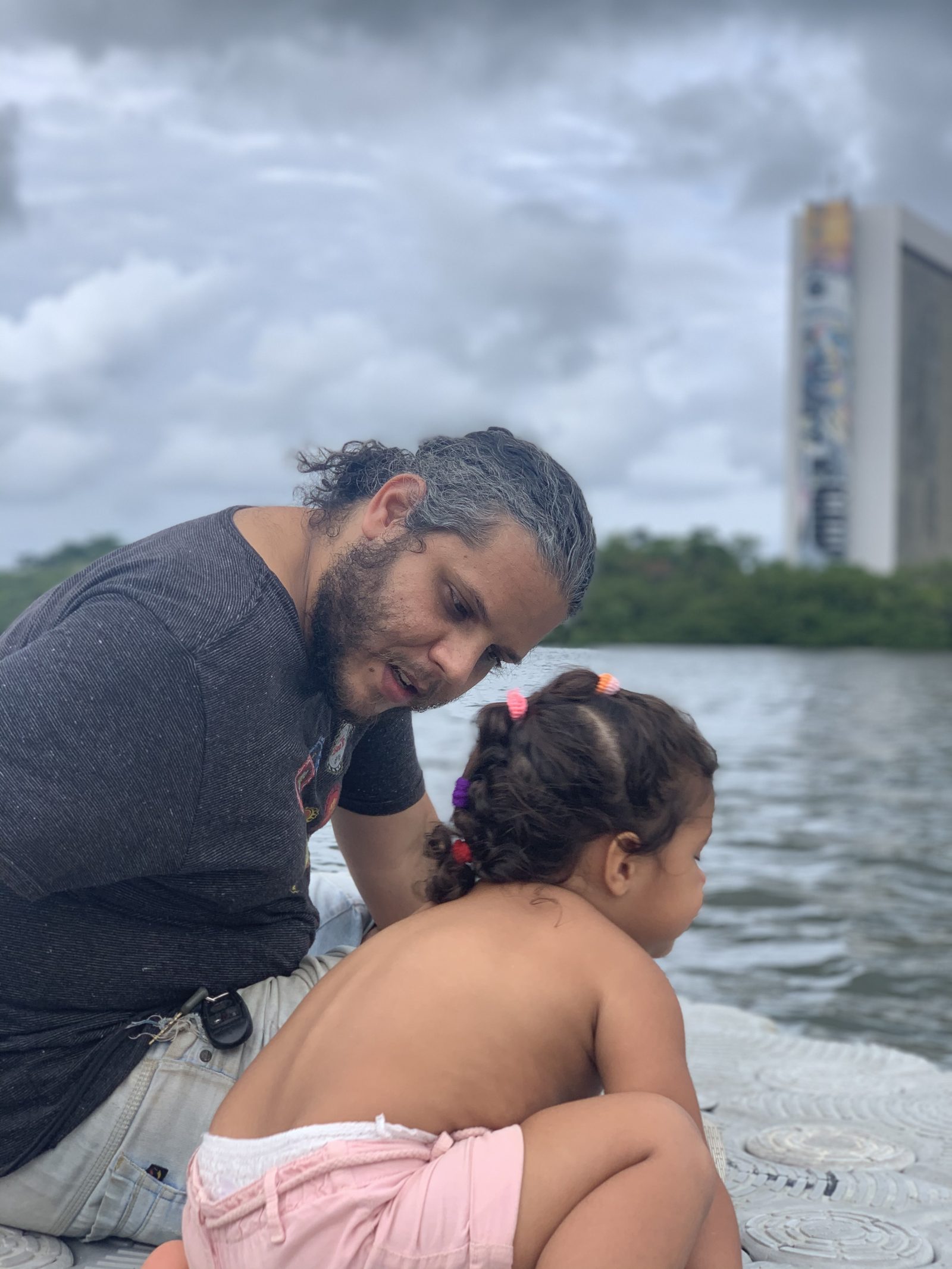 Igor e a filha Maria Anita num barco no rio, com a cidade do Recife ao fundo