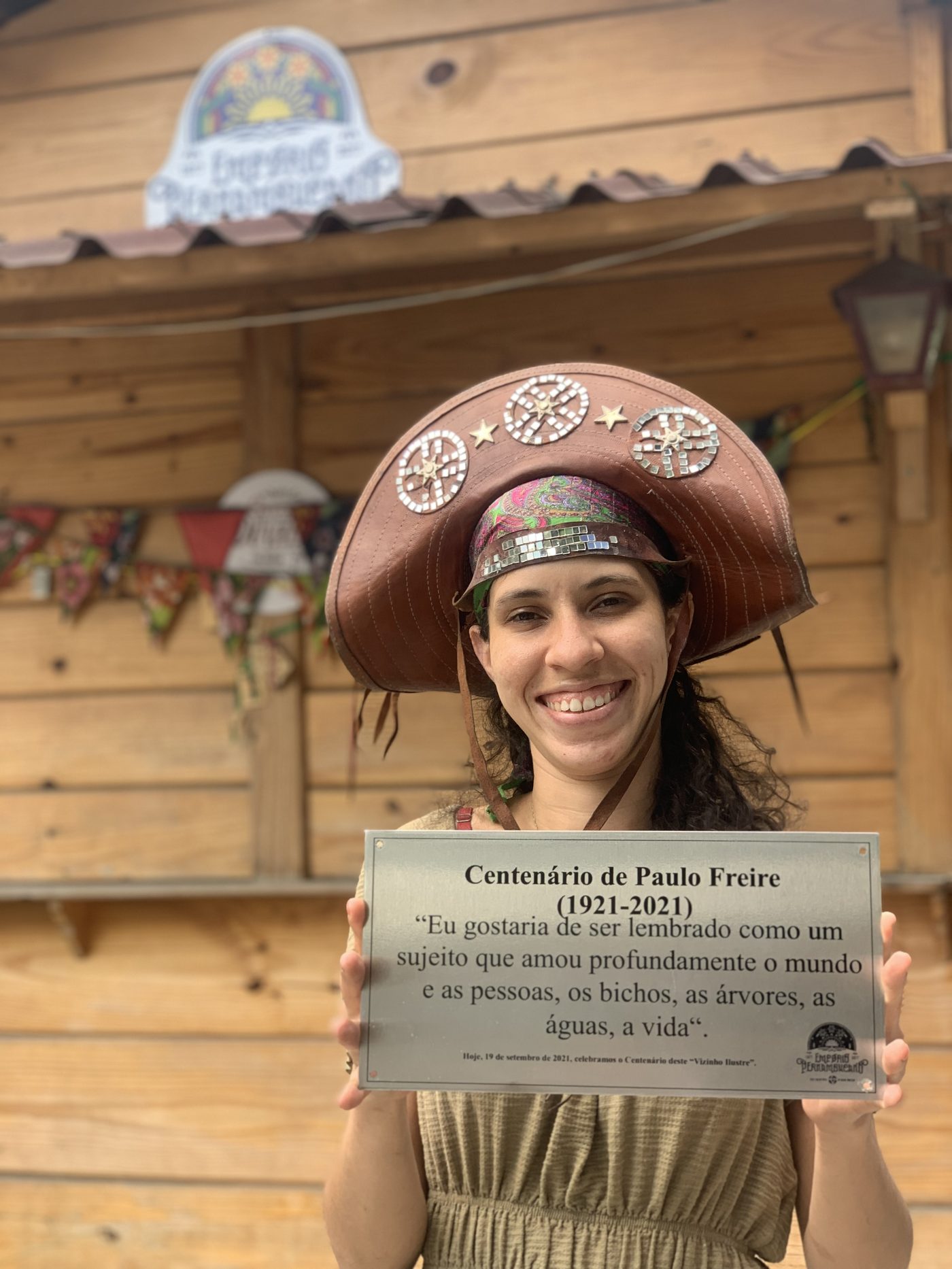 Laysa segurando a placa em homenagem ao centenário de Paulo Freire, na loja do Empório
