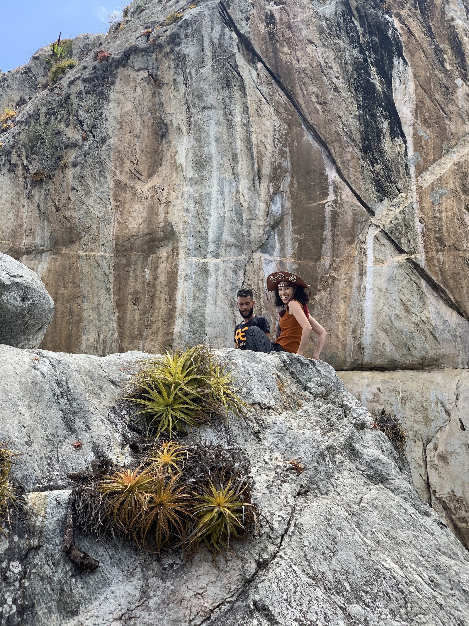 Laysa e Igor sentados no paredão de pedra, entre bromélias da caatinga